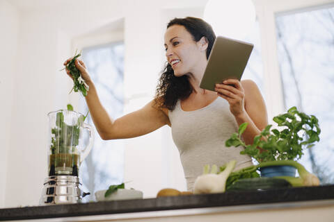 Eine fitte Frau steht in der Küche und bereitet einen gesunden Smoothie nach einem Online-Rezept zu, lizenzfreies Stockfoto