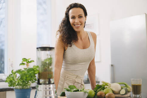 Fitte Frau steht in der Küche und bereitet einen gesunden Smoothie zu - JOSEF00030
