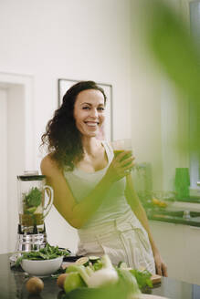 Fitte Frau steht in der Küche und trinkt einen gesunden Smoothie - JOSEF00031