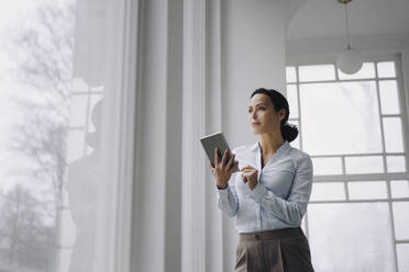 Successful businesswoman, standing by window, using digital tablet - JOSEF00032