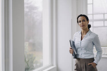 Successful businesswoman, standing by window, carrying laptop - JOSEF00034