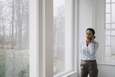 Successful businesswoman, standing by window, talking on the phone - JOSEF00038