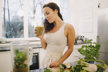 Fitte Frau steht in der Küche und bereitet einen gesunden Smoothie zu - JOSEF00046