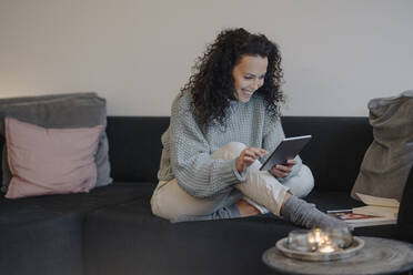 Woman sitting at home on couch, using digital tablet, reading - JOSEF00053