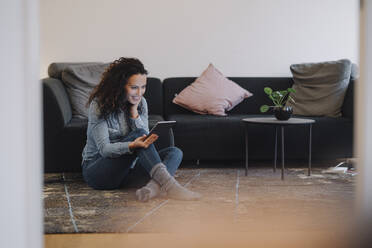 Woman sitting at home on floor, using digital tablet, reading - JOSEF00065