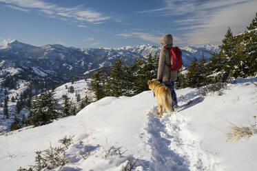 Weiblicher Wanderer und Hund schauen in die Ferne in einer verschneiten Berglandschaft - CAVF75572