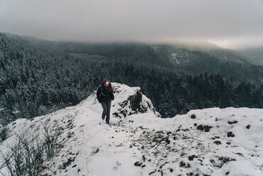 A young woman walks to the top of a snowy point in the Columbia Gorge - CAVF75674