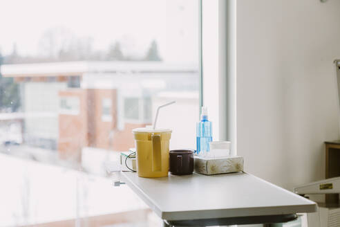 Gegenstände auf dem Nachttisch in einem Krankenhauszimmer mit Fenster im Hintergrund - CAVF75772