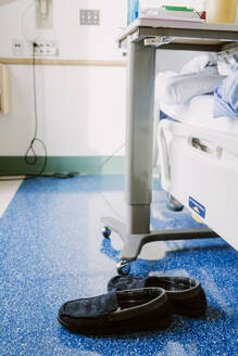 Marineblaue Hausschuhe auf dem Boden im Krankenhauszimmer neben Bett und Tisch - CAVF75773