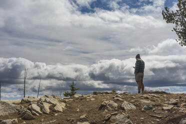 Männlicher Wanderer auf einem Berg stehend mit Handy und dramatischen Wolken - CAVF75800