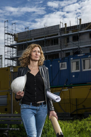 Architektin mit Helm und Bauplan auf der Baustelle, lizenzfreies Stockfoto