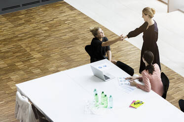 Businesswomen shaking hands in modern office conference room - BMOF00289