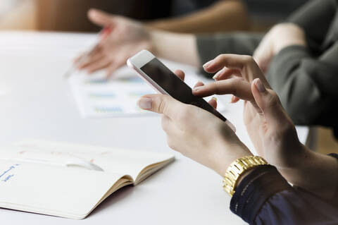 Nahaufnahme einer Geschäftsfrau, die während einer Besprechung im Büro ein Smartphone benutzt, lizenzfreies Stockfoto