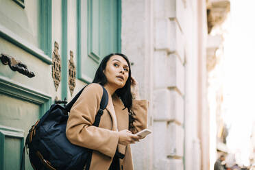 Porträt einer modischen jungen Frau mit Rucksack und Mobiltelefon, Lissabon, Portugal - DCRF00012