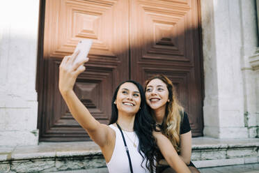 Porträt von zwei glücklichen jungen Frauen, die ein Selfie mit ihrem Smartphone machen, Lissabon, Portugal - DCRF00015