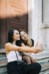 Portrait of two freinds sitting on stairs taking selfie with smartphone, Lisbon, Portugal - DCRF00017