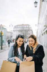 Zwei junge Frauen mit Einkaufstaschen in der Stadt, Lissabon, Portugal - DCRF00023