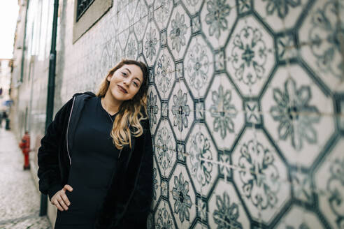 Portrait of happy young woman dressed in black leaning against Azulejo wall, Lisbon, Portugal - DCRF00031