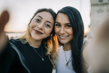 Portrait of two happy friends takind selfie head to head at sunset, Lisbon, Portugal - DCRF00042