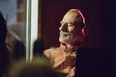 Relaxed businessman taking a break, listening music with headphones in his sustainable office - MCF00555