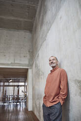 Creative businessman leaning against wall in his minimalistic office - MCF00566