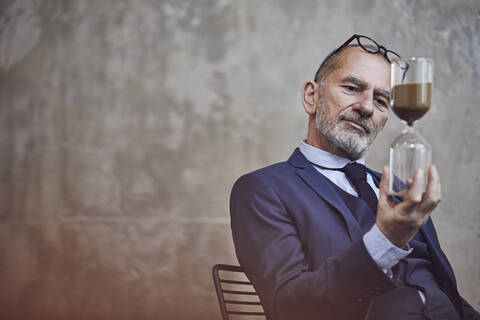 Senior businessman watching sand, trickling through hourglass stock photo