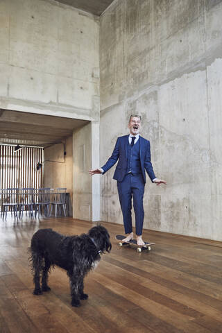 Senior businessman skateboarding in his office, dog is watching stock photo