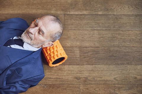 Älterer Geschäftsmann entspannt auf Holzboden, auf Faszienrolle ruhend, lizenzfreies Stockfoto