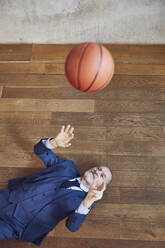 Senior Geschäftsmann auf Holzboden liegend, mit Basketball spielend - MCF00618