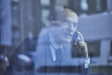Senior businessman, looking out of window, talking on the phone - MCF00622