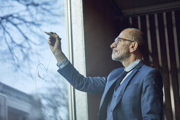 Senior-Geschäftsmann zeichnet Diagramm auf Fensterscheibe - MCF00623