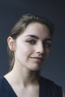 Porträt einer lächelnden jungen Frau vor grauem Hintergrund - KNSF07621