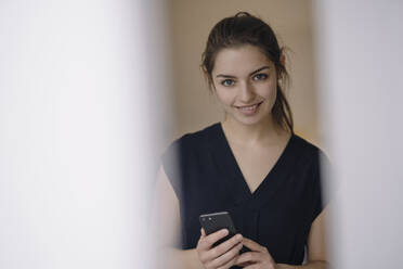 Porträt einer lächelnden jungen Frau mit Mobiltelefon - KNSF07642