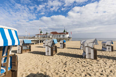 Germany, Mecklenburg-Western Pomerania, Heringsdorf, Hooded beach chairs on sandy coastal beach with pier in background - WDF05840