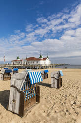 Germany, Mecklenburg-Western Pomerania, Heringsdorf, Hooded beach chairs on sandy coastal beach with pier in background - WDF05841