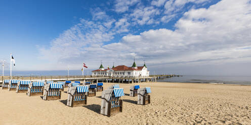 Deutschland, Mecklenburg-Vorpommern, Heringsdorf, Strandkörbe mit Kapuze am sandigen Küstenstrand mit Seebrücke im Hintergrund - WDF05842