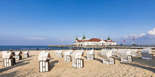 Deutschland, Mecklenburg-Vorpommern, Heringsdorf, Strandkörbe mit Kapuze am sandigen Küstenstrand mit Seebrücke im Hintergrund - WDF05843