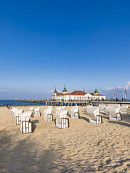 Germany, Mecklenburg-Western Pomerania, Heringsdorf, Hooded beach chairs on sandy coastal beach with pier in background - WDF05844