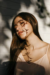 Portrait of teenage girl with shadow of leaves on her face - TCEF00192