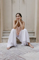 Portrait of melancholic teenage girl wearing white culottes sitting barefoot on steps outdoors - TCEF00210