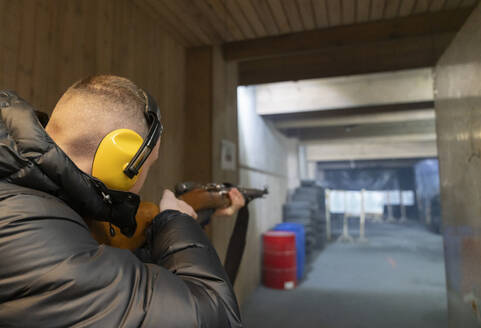 Young man aiming with a gun in shooting range - AHSF01969