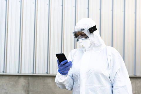 Wissenschaftlerin mit Schutzanzug und Maske, die auf ein Smartphone schaut, lizenzfreies Stockfoto