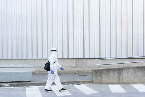 Female scientist wearing protective suit and mask and walking in front of a laboratory - ERRF02738