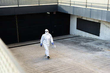 Female scientist wearing protective suit and mask and walking at a garage - ERRF02743