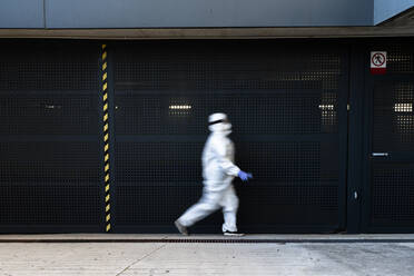 Wissenschaftlerin mit Schutzanzug und Maske, die vor einer Wand läuft - ERRF02745