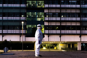 Female scientist wearing protective suit and mask and standing in front of a laboratory - ERRF02751