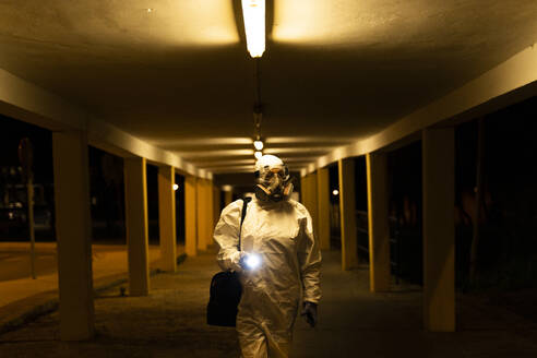 Senior woman wearing protective suit and mask in the city at night - ERRF02760