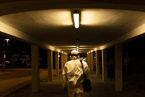 Senior woman wearing protective suit and mask in the city at night - ERRF02761