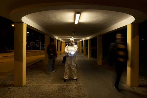 Senior woman wearing protective suit and mask in the city at night - ERRF02762
