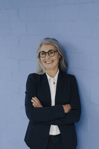 Portrait of smiling grey-haired businesswoman standing at a blue wall stock photo